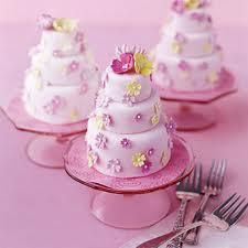 Pink tiered cakes decorated with flowers on matching pink cake stands and forks nearby
