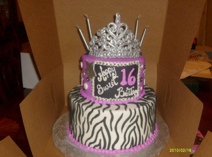 Purple zebra-print birthday cake with silver tiara topper and a “16” plaque in a cardboard box