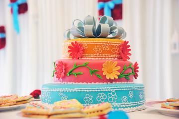 Colorful tiered celebration cake with a silver bow topper on a decorated table, surrounded by treats