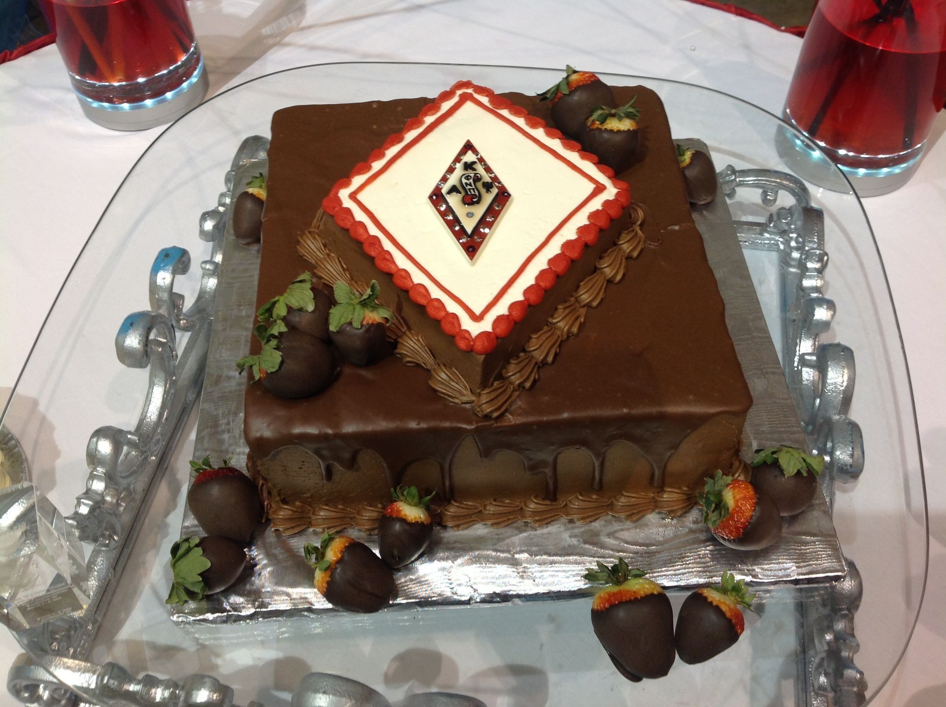 Chocolate layered cake with white and red icing, decorated with fruit on a serving tray