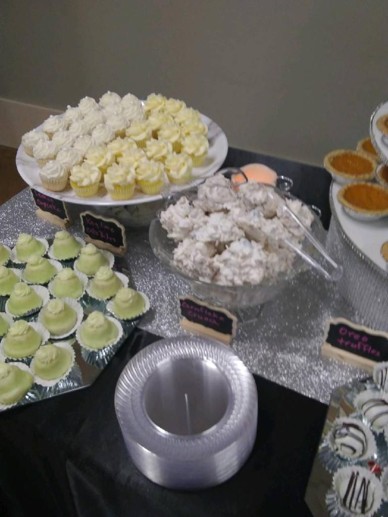 Assorted frosted cupcakes and desserts on a buffet table with tongs and a silver bowl