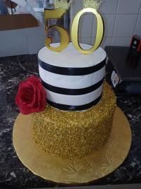 Gold and black striped cake with red rose and gold “50” topper on a gold board