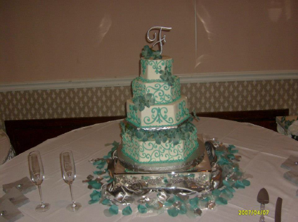 Tiered white-and-teal wedding cake on a decorated table with candles and place settings.