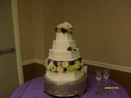Three-tier white wedding cake with purple and white flowers on a purple tablecloth