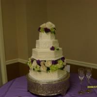 Three-tier white wedding cake with purple and white flowers on a table in a banquet room