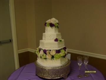 Three-tier white wedding cake with purple and green floral accents on a purple tablecloth