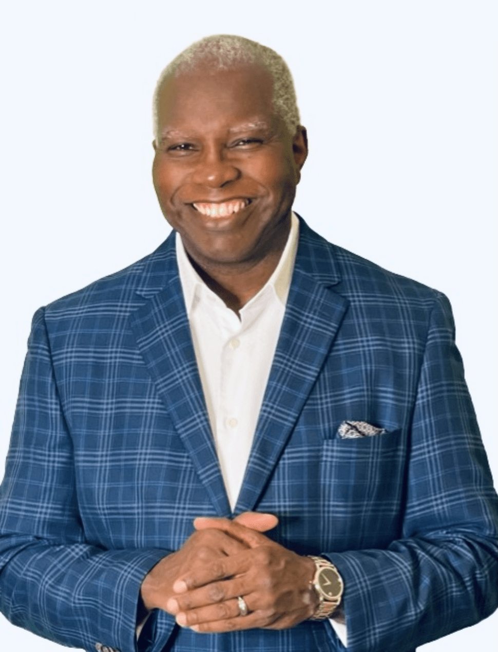 A man in a blue plaid suit is smiling with his hands folded.