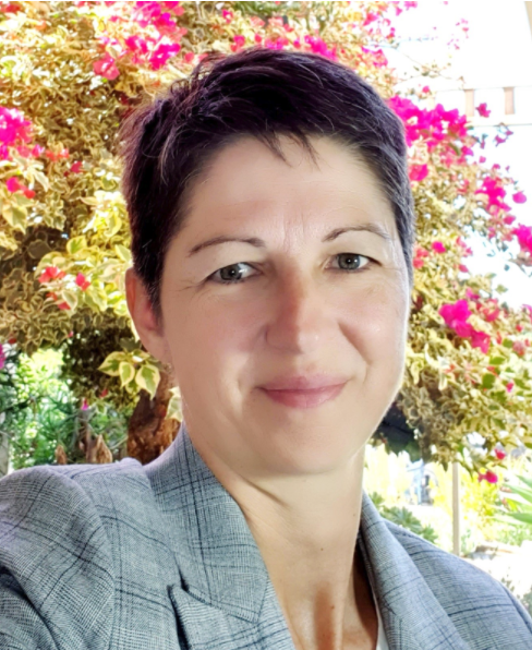 A woman in a suit is smiling in front of a tree with pink flowers.