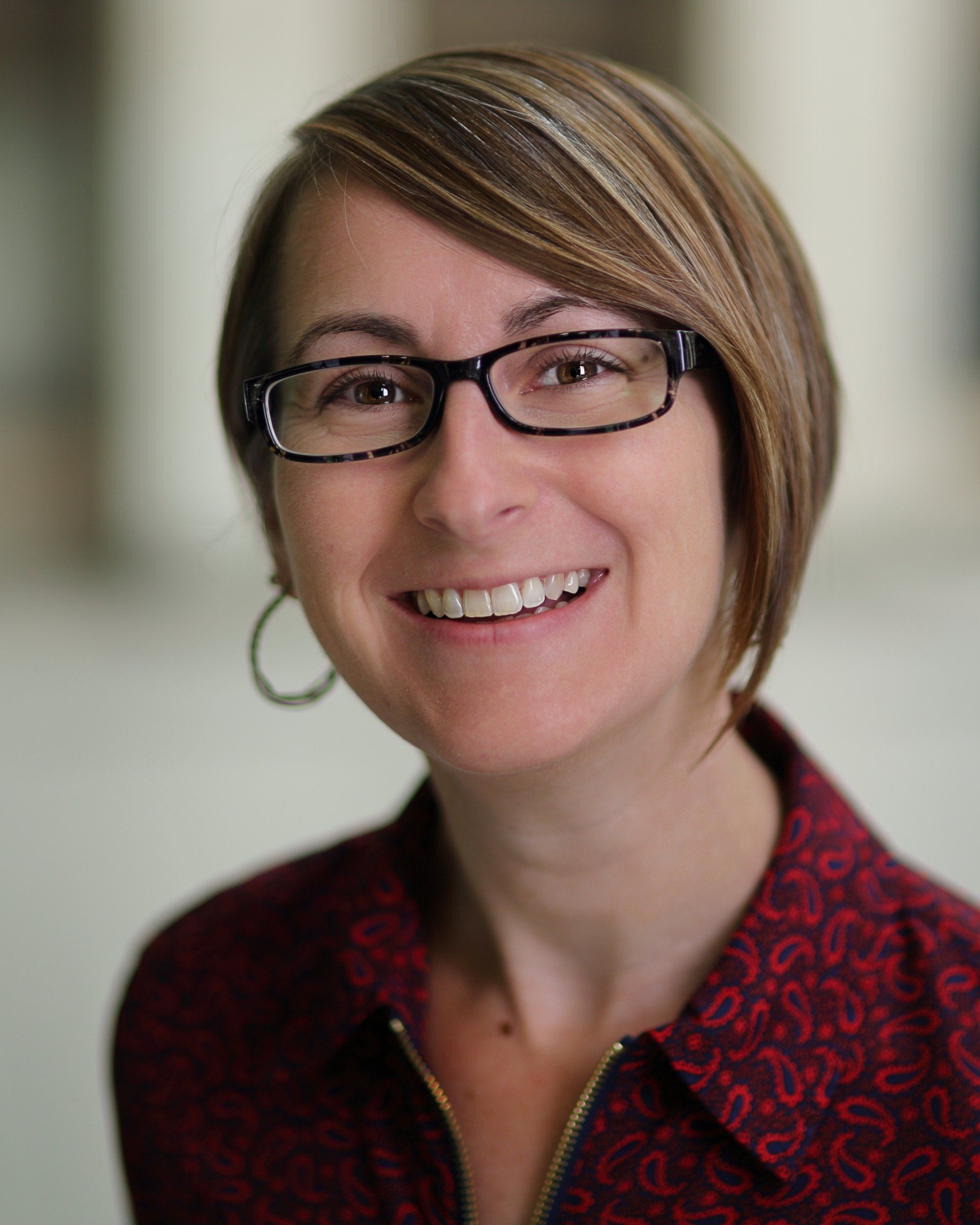A woman wearing glasses and a red shirt is smiling for the camera.