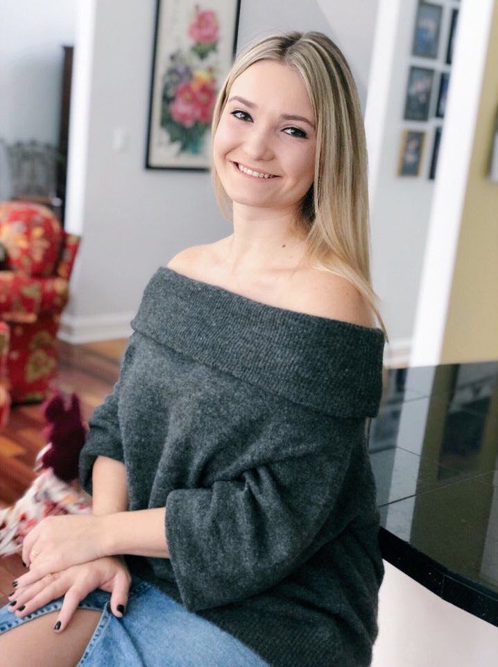 A woman in a grey off the shoulder sweater is sitting on a bar.