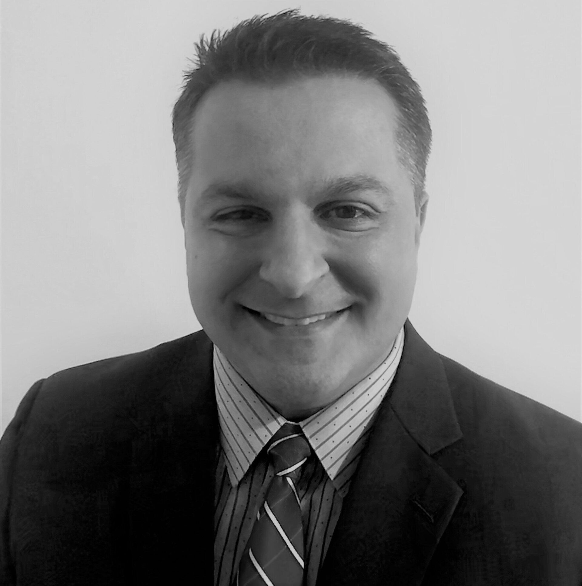 A black and white headshot of Michael Delis, A white man with short dark hair, wearing a coat and tie.