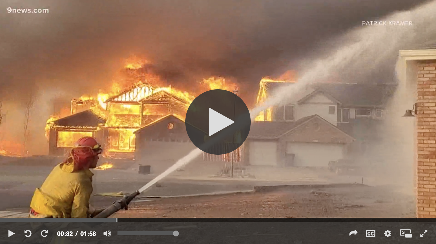 A firefighter spraying water onto a burning house.
