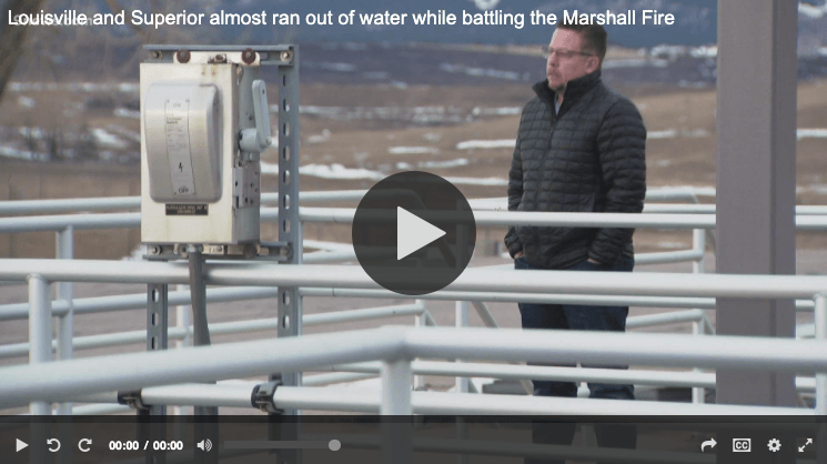 A video still with a man standing on an outdoor deck in a winter coat