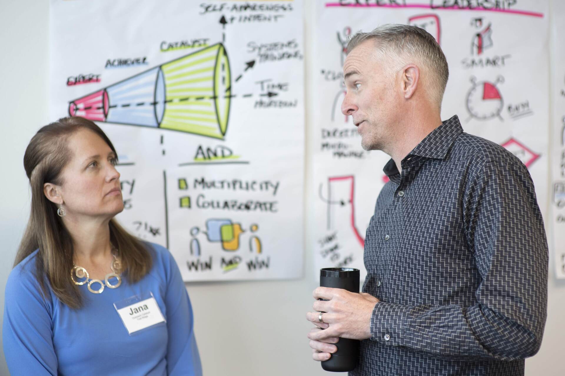 A man and a woman are standing next to each other in front of a whiteboard.