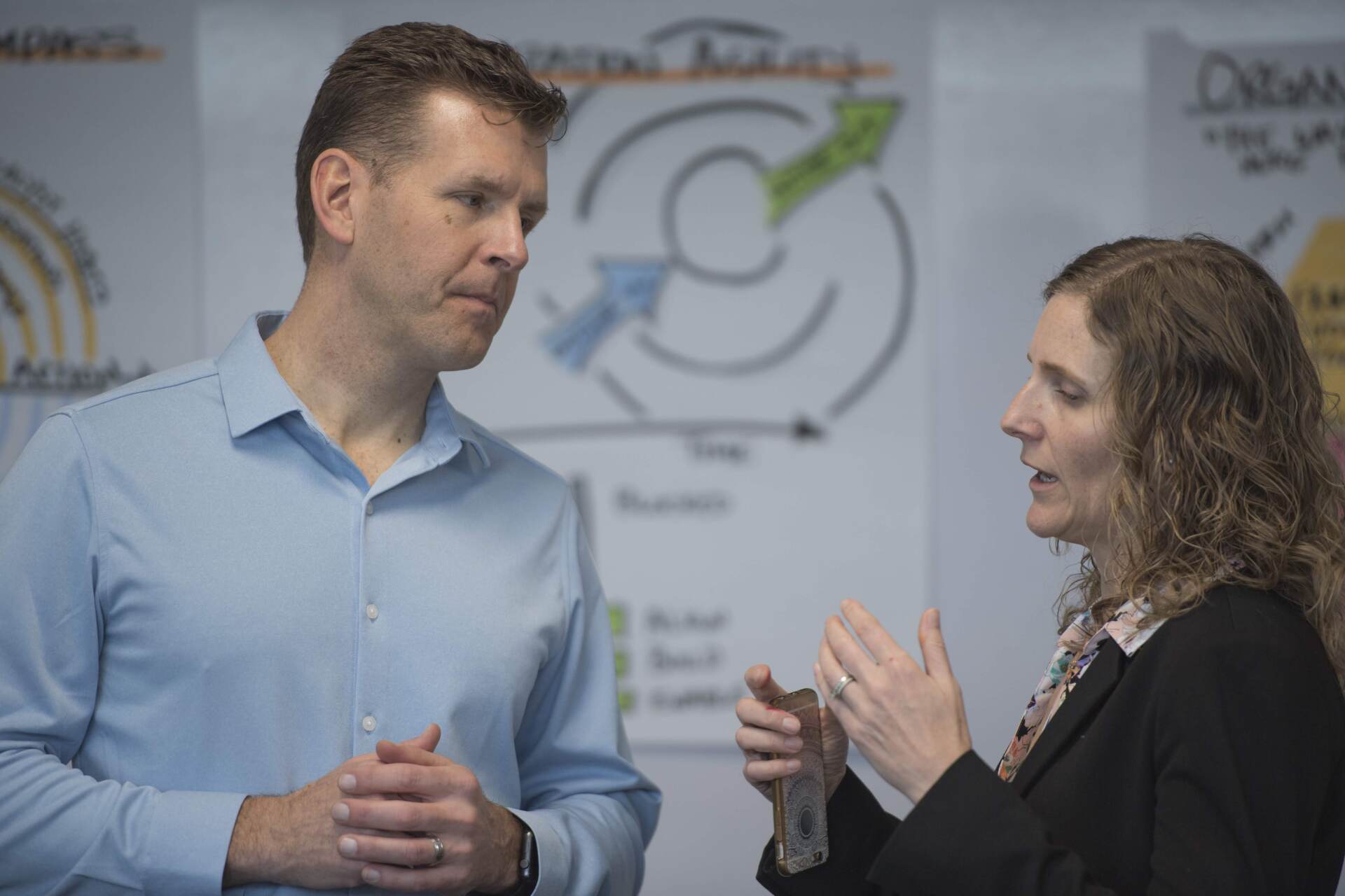 A man and a woman are talking to each other in front of a whiteboard.