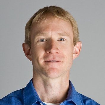 A headshot of Brad Swanson, a light skinned man with blonde hair. Brad is wearing a blue collared shirt and smiling slightly.
