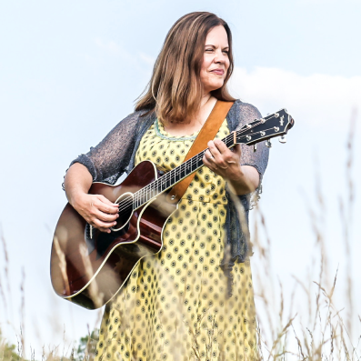 A woman in a yellow dress is holding a guitar in a field.