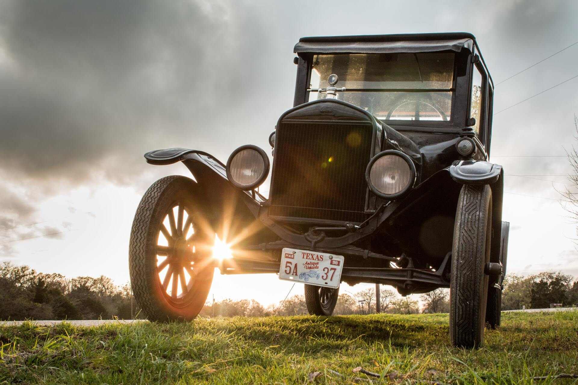 A Ford Model T drives across a green field. The setting sun shines between the ground and the tire.