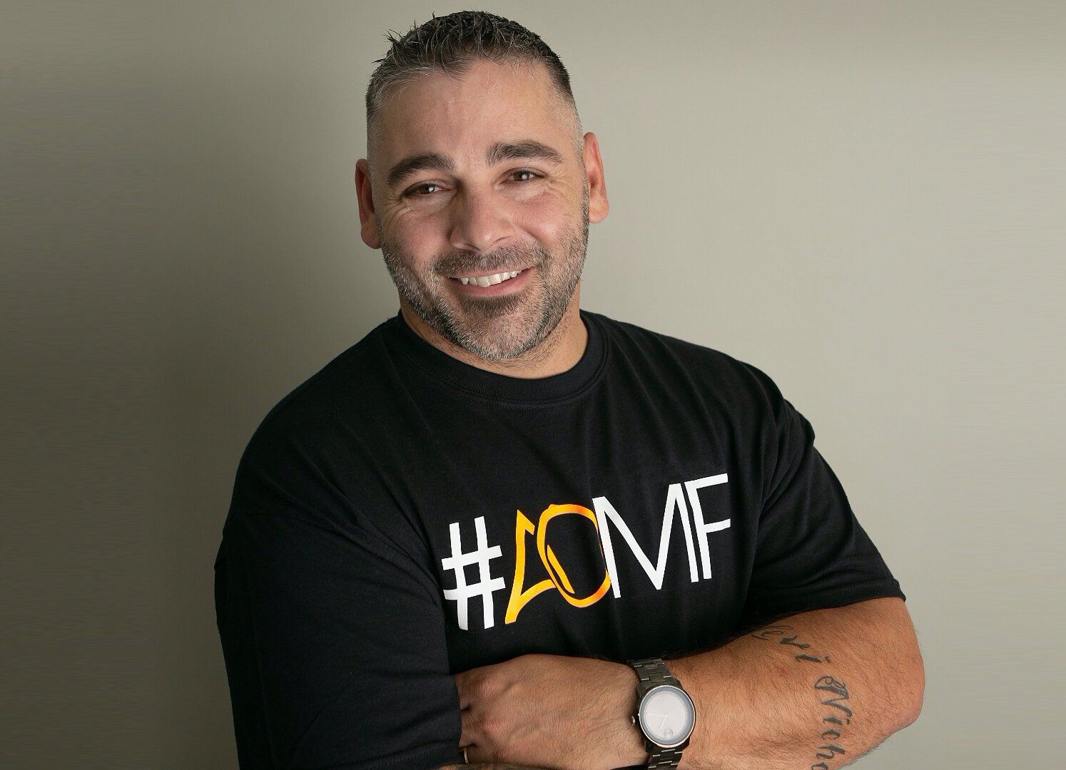 A color photograph of Nick Berendt, who is posing with his arms crossed and is wearing a black t-shirt