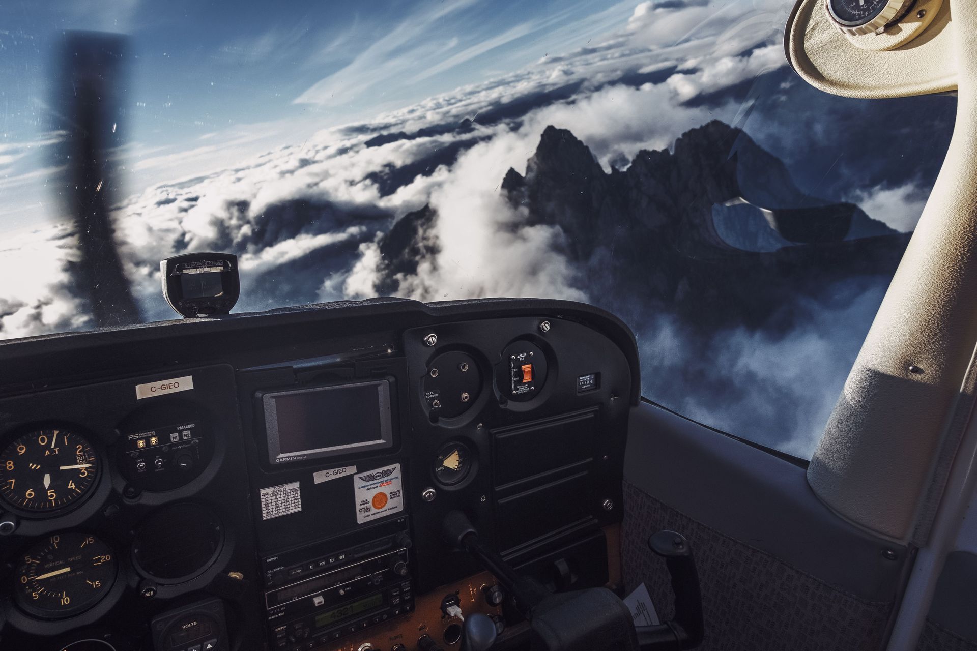 Aircraft cockpit above clouds with peaks ahead. Flying by instruments, not sight.