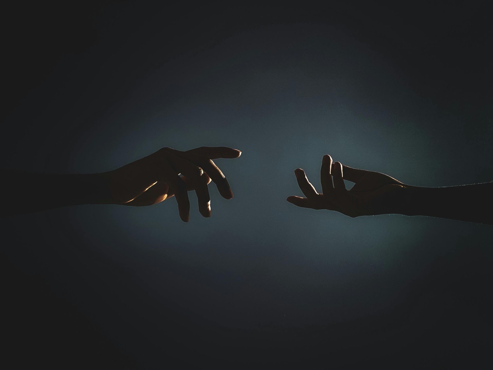 Two hands reaching toward each other in a dark, dimly lit scene with a glowing blue center