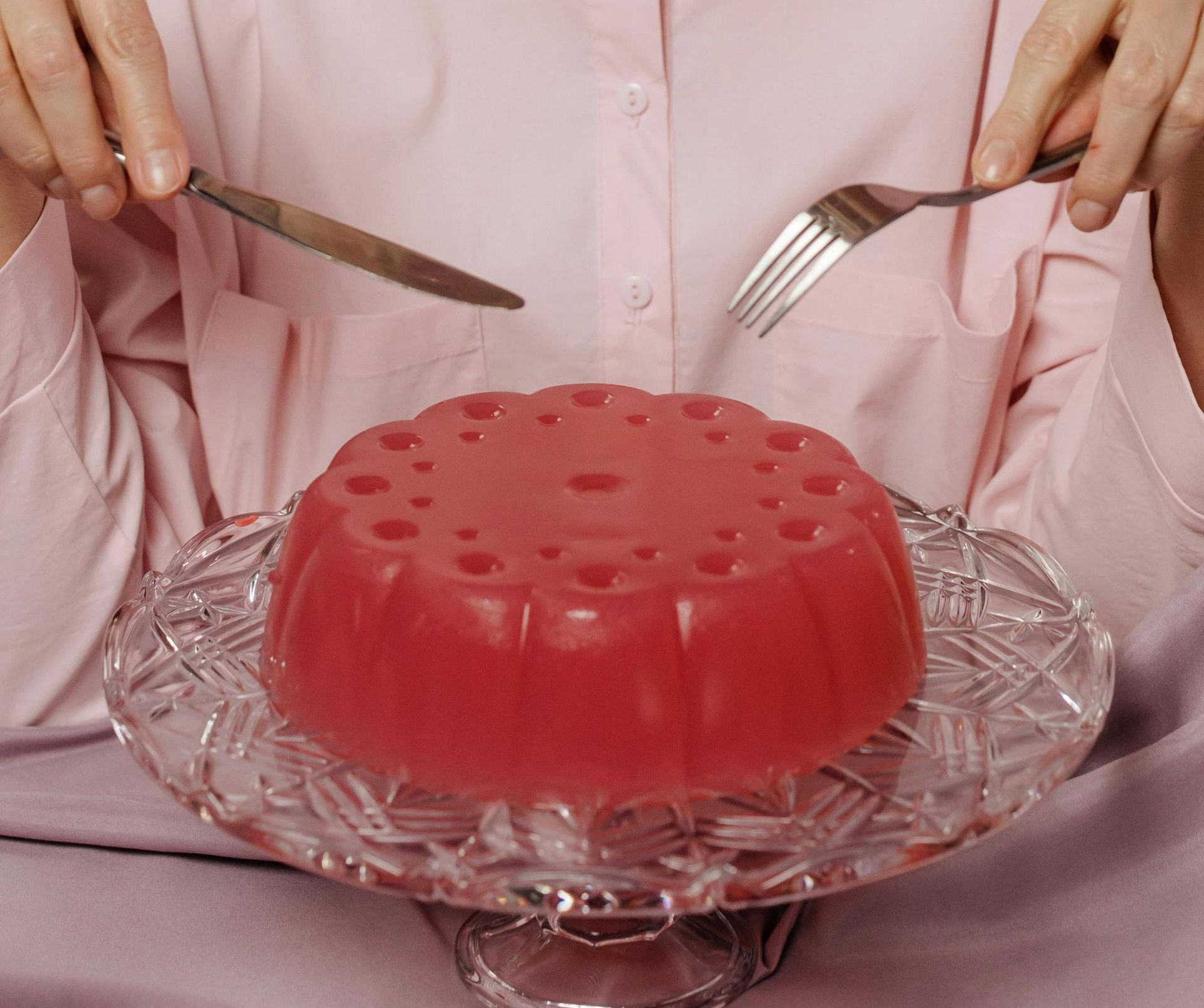 A woman is cutting a piece of red jelly with holes in it
