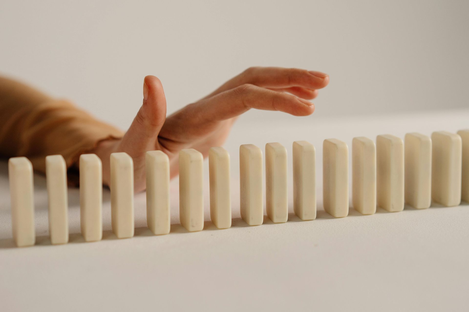 A person 's hand is reaching for a row of dominoes.