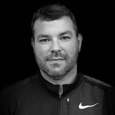 A black and white photo of a man with a beard wearing a nike jacket.