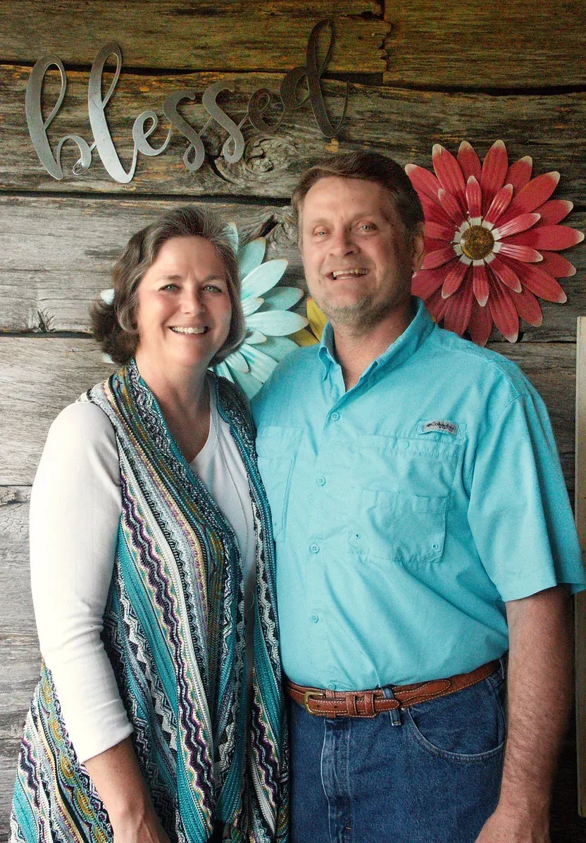 A man and a woman are posing for a picture in front of a wooden wall.