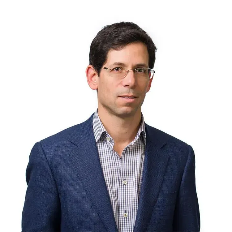 A man wearing glasses and a blue suit is standing in front of a white background.