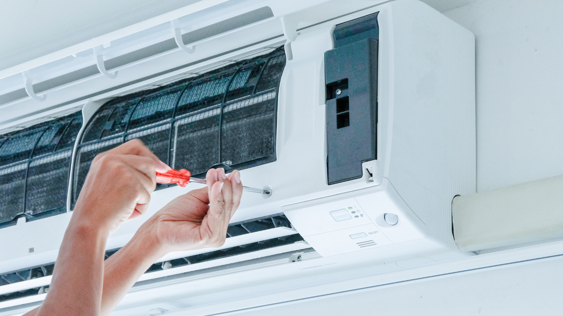 A person is fixing an air conditioner with a screwdriver.