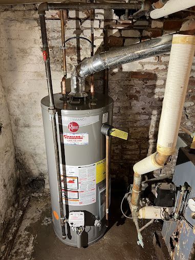 A water heater is sitting in a basement next to a boiler.
