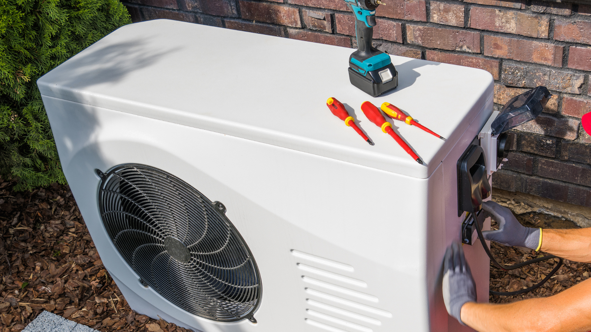 A person is working on an air conditioner outside of a brick building.