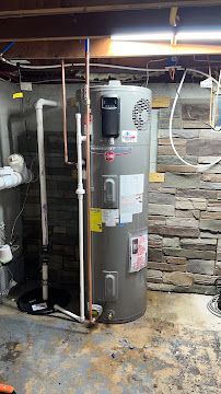 A water heater is sitting in a basement next to a stone wall.