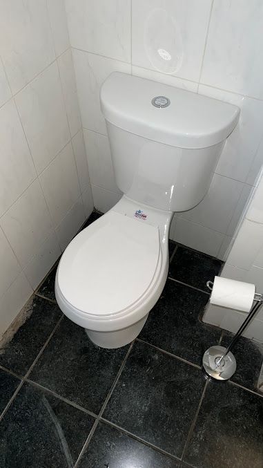 A white toilet is sitting on a black tiled floor in a bathroom.