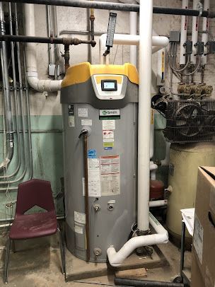 A large water heater is sitting in a room next to a chair.