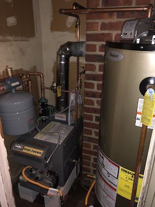 A water heater is sitting in a room next to a brick wall.