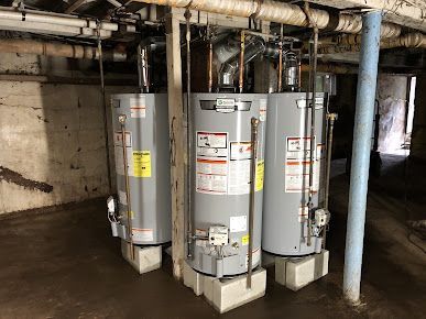 Three water heaters are sitting next to each other in a basement.