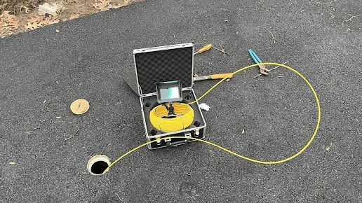 A drain camera is sitting on the ground next to a briefcase.