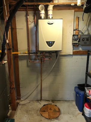 A water heater is installed in a basement next to a brick wall.