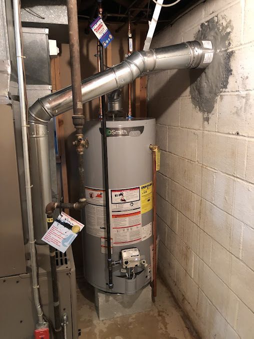 A water heater is sitting in a basement next to a brick wall.
