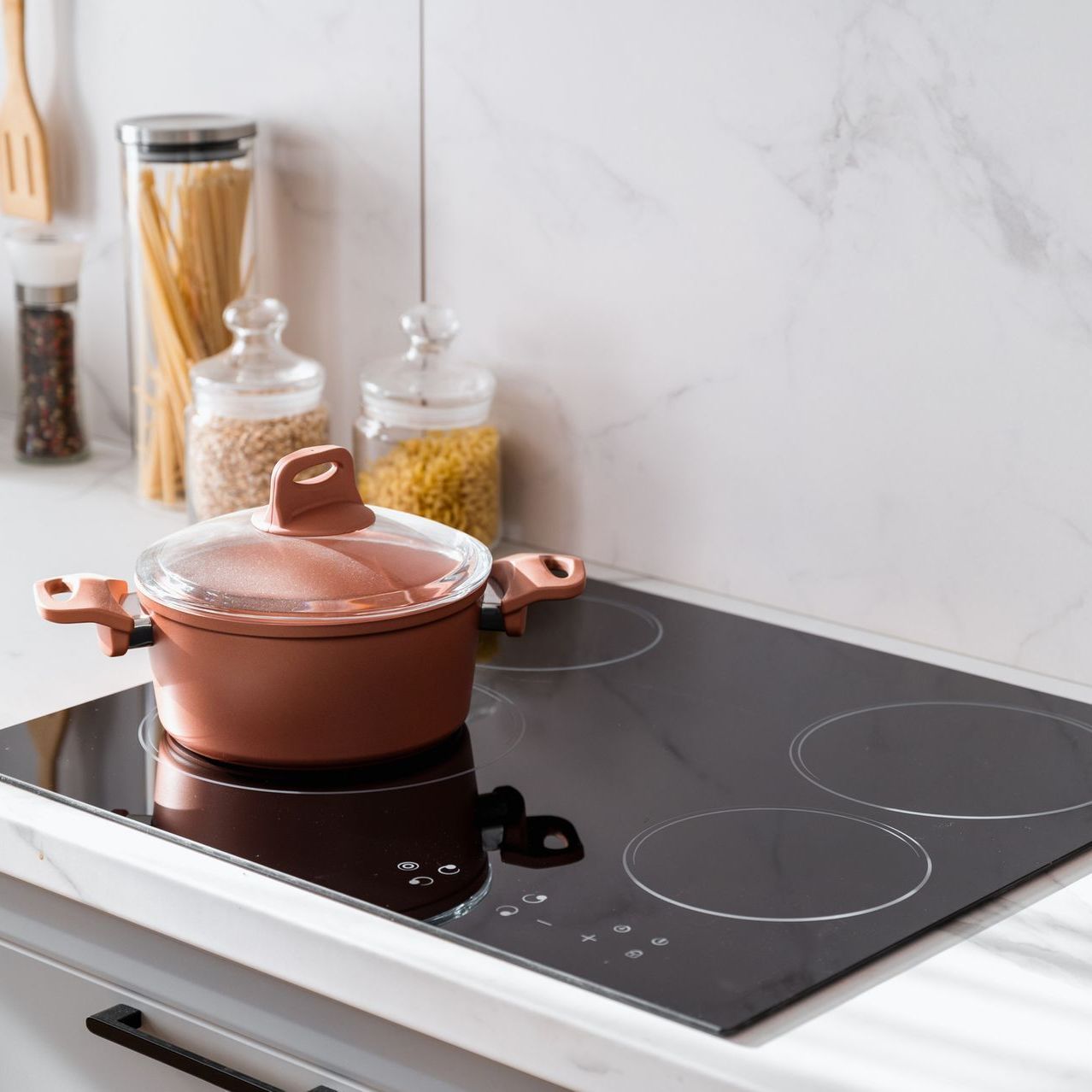 Copper-colored pot with lid on a black cooktop in a kitchen setting.