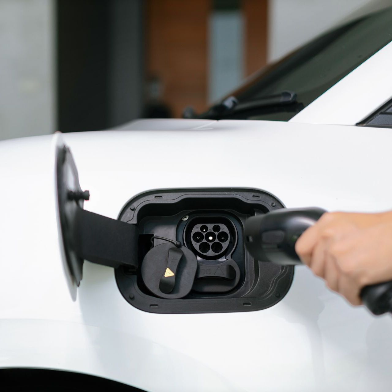 White electric car charging port with a hand plugging in the charging cable.