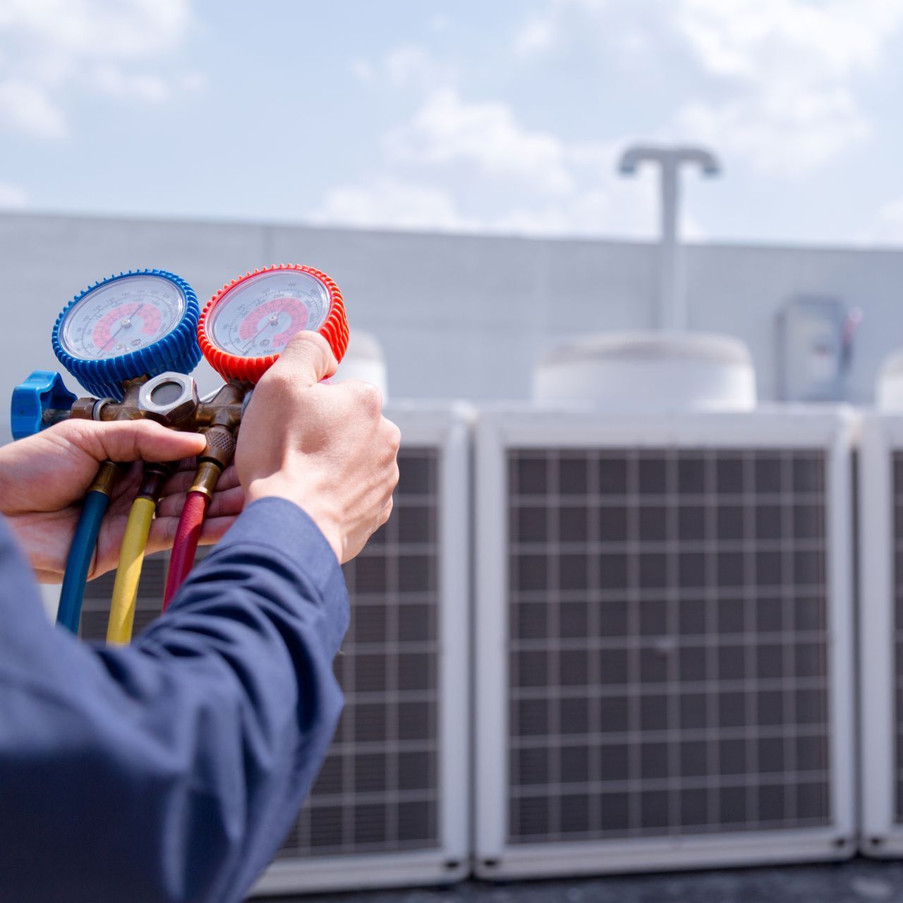 HVAC technician holding gauges, checking air conditioning units on a rooftop.