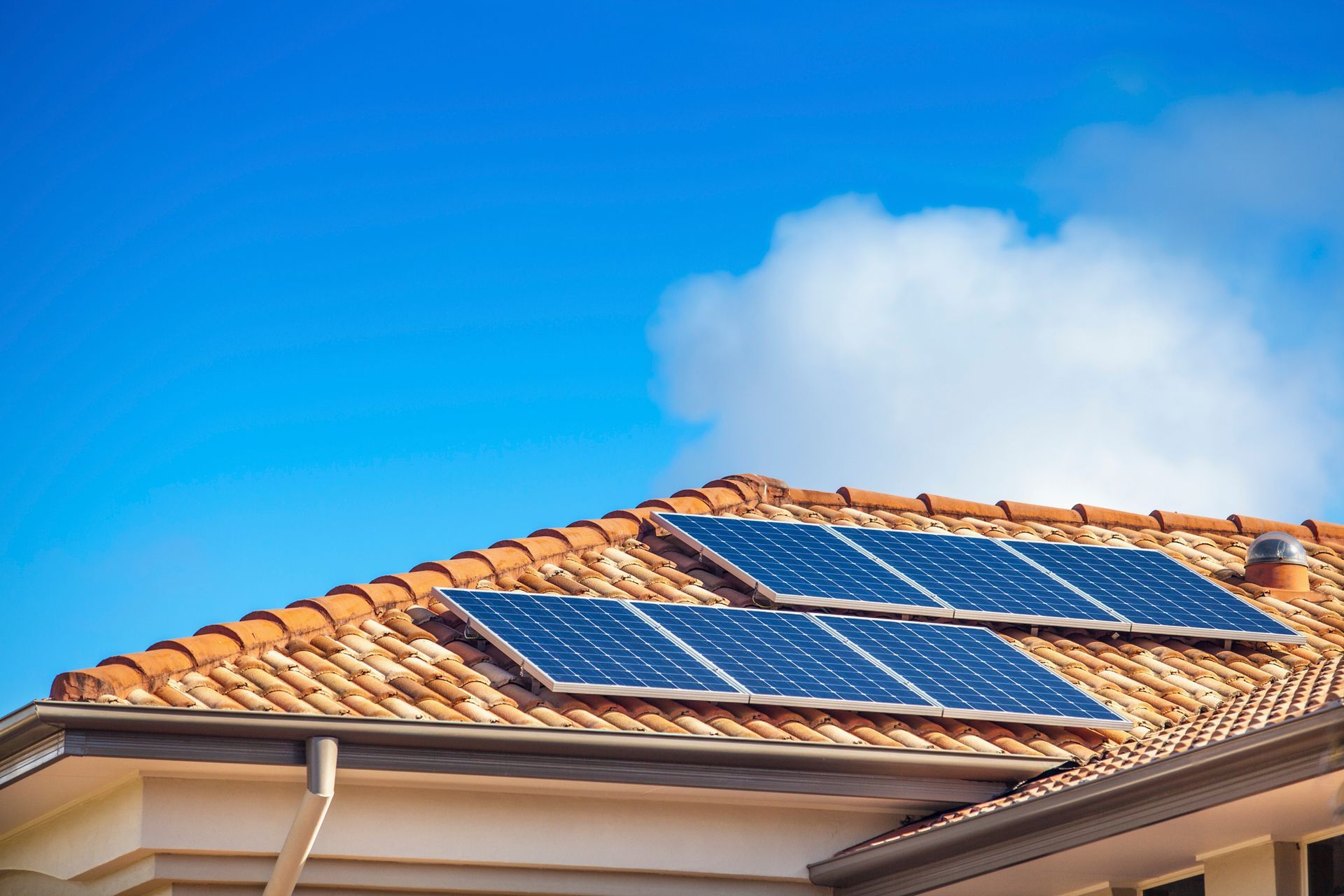 Solar panels on a terracotta tile roof against a blue sky with clouds.