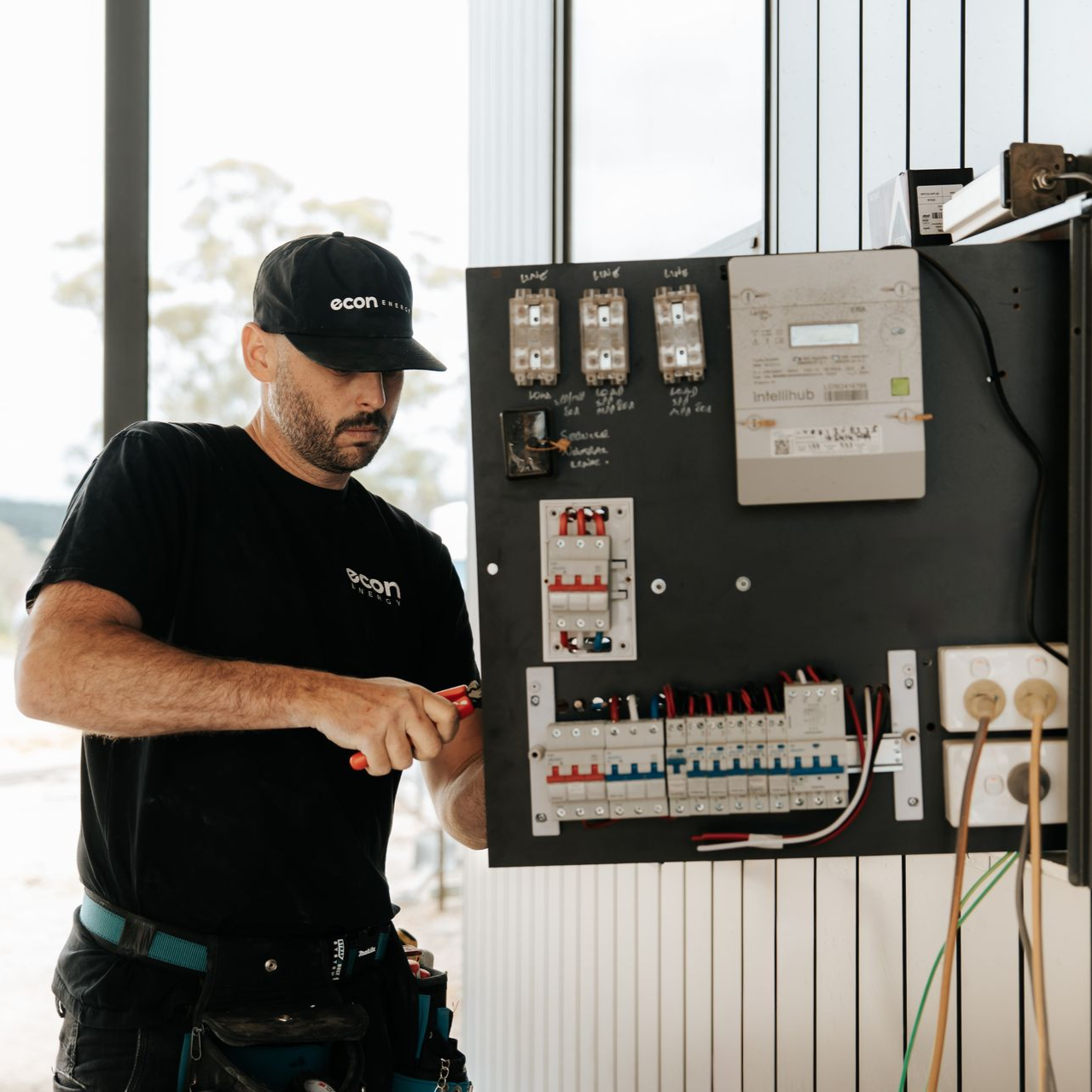 Electrician using pliers on wires in a circuit breaker panel.