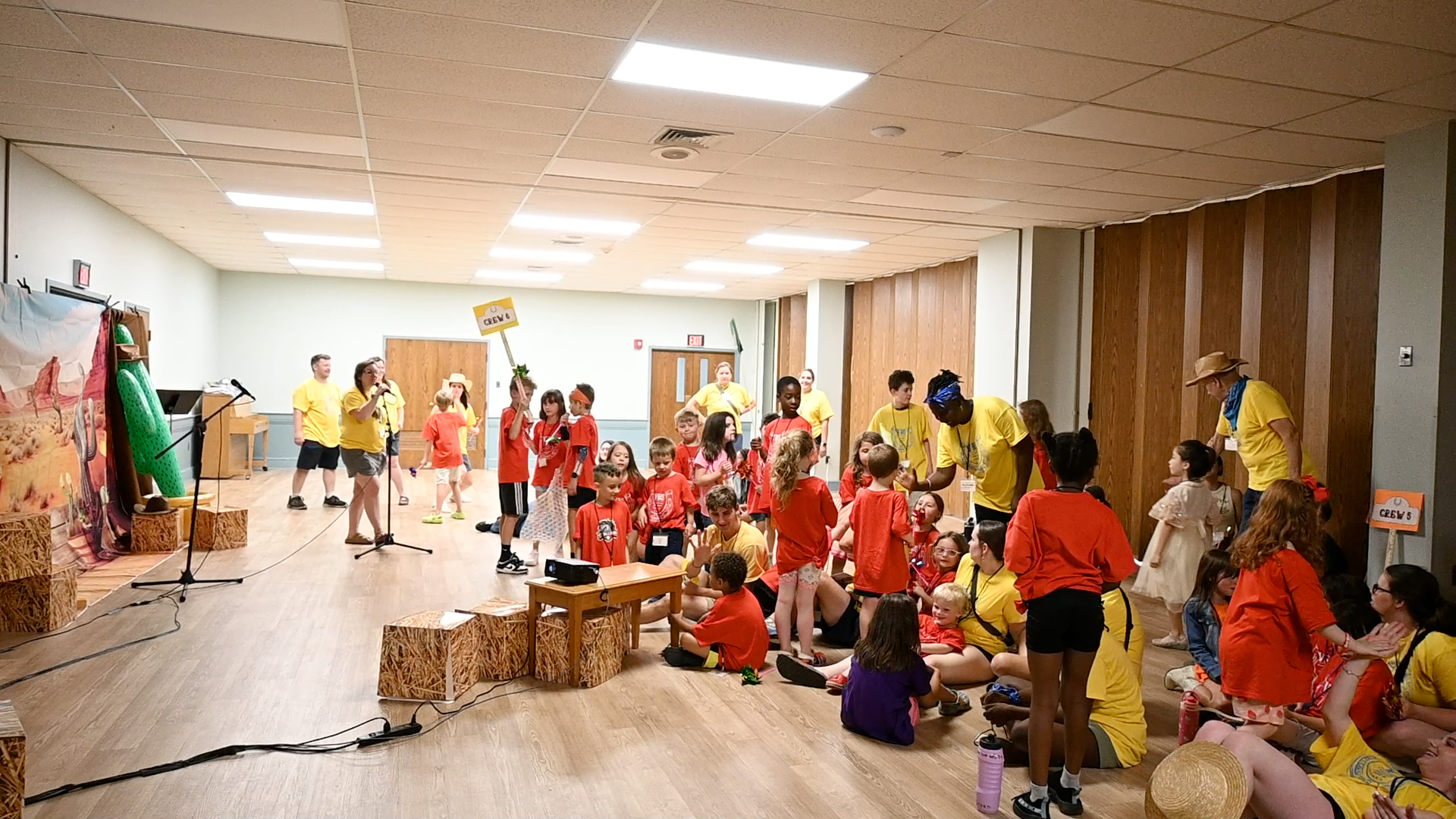 Children in red shirts gather in a bright room with baskets, crafts, and decorations.