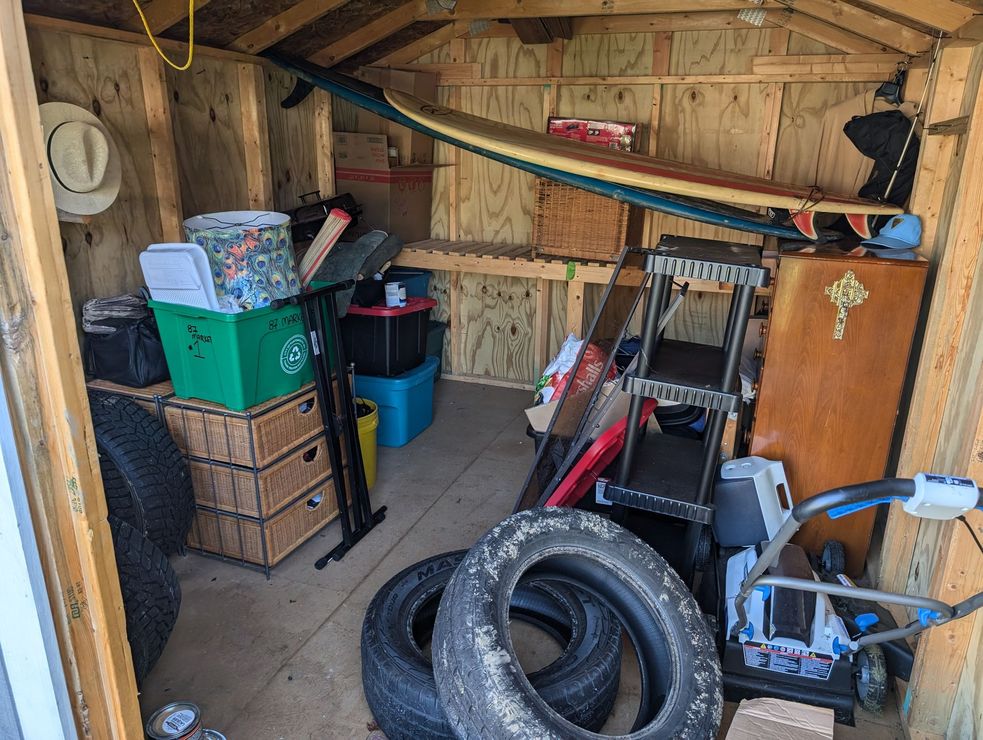 A shed filled with lots of items including tires and a surfboard.