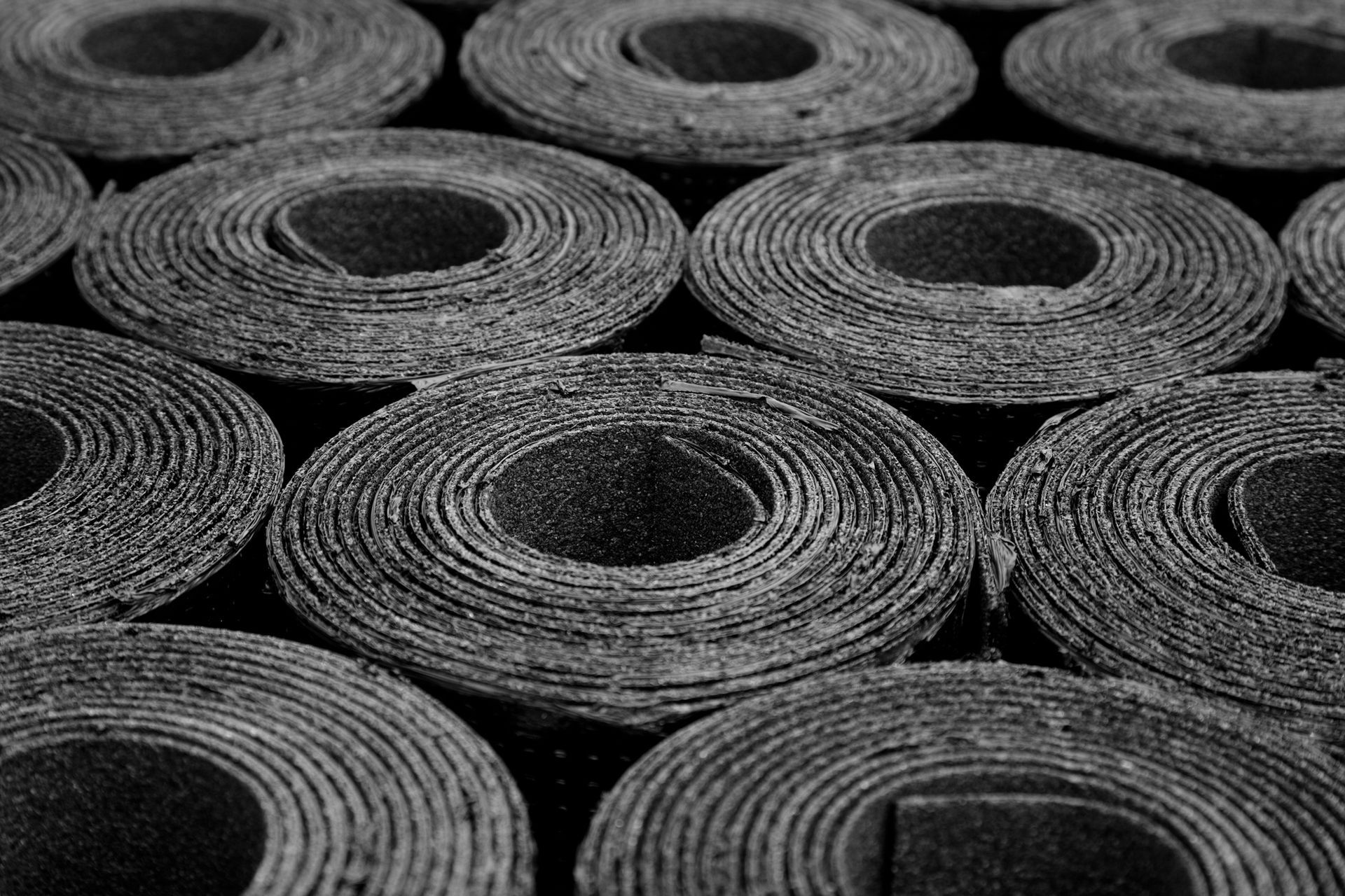 Una vista monocromatica dall'alto di diversi rotoli strettamente avvolti di materiale per coperture industriali o feltro bituminoso.