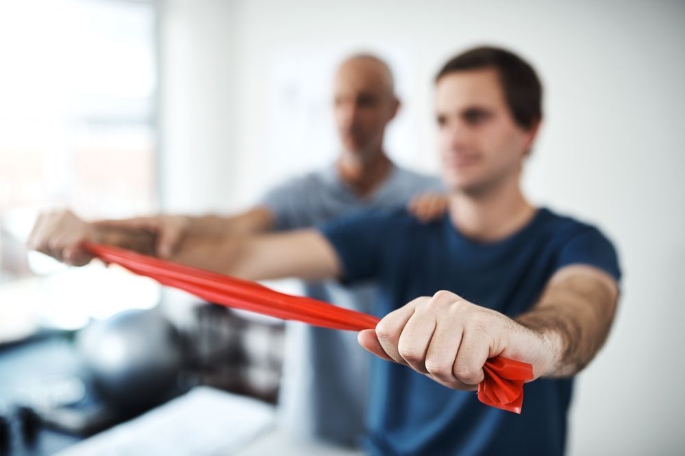 A Man is Doing Exercises With a Red Resistance Band — Body In Motion Physiotherapy in Pialba, QLD